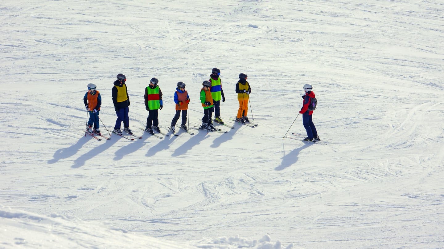 Un maestro di sci insegna a bambini con giubbotti colorati su pendii innevati.