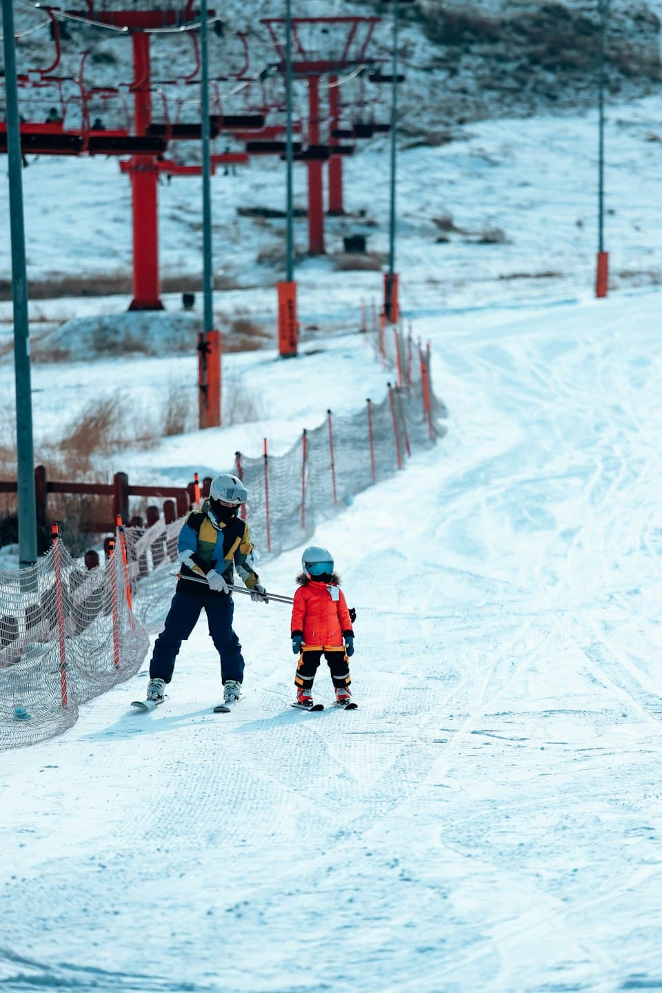 Un adulto sciatore guida un bambino su un pendio innevato.