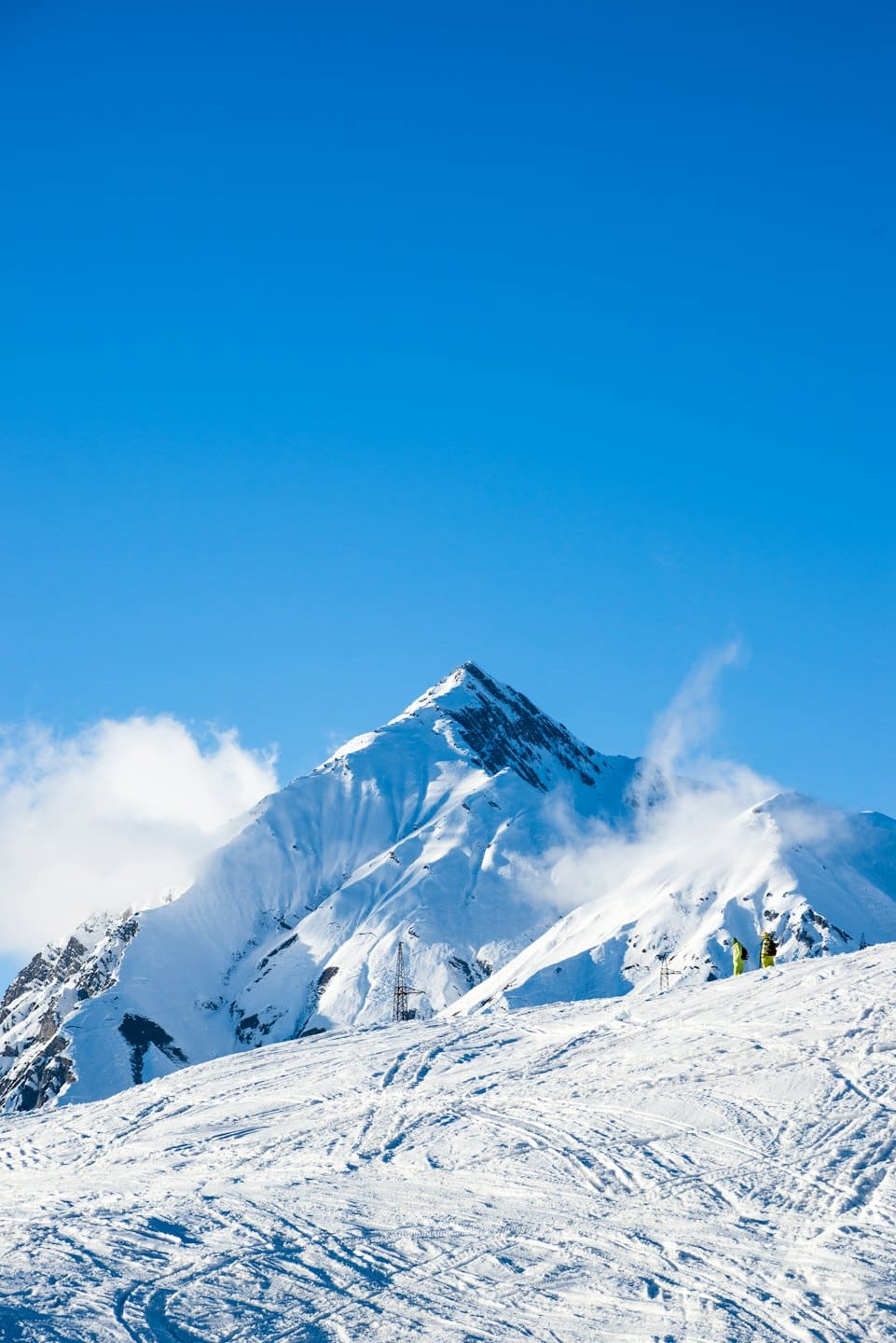 Due sciatori si trovano su un vasto pendio montano innevato.